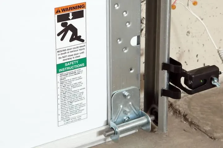 Garage door track, roller, and safety sensor being repaired in a Little Rock garage